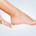 Perfect clean female feet . Woman touching her smooth heel, on blue background, closeup