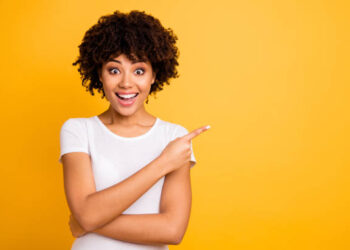 Portrait of her she nice cute lovely charming attractive cheerful cheery glad optimistic wavy-haired girl pointing aside copy space isolated on bright vivid shine yellow background.