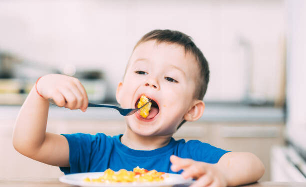a child in a t-shirt in the kitchen eating an omelet, a fork