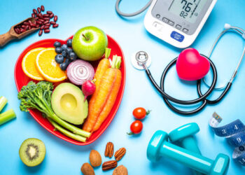Healthy lifestyle concepts: red heart shape plate with fresh organic fruits and vegetables shot on blue background. A digital blood pressure monitor, doctor stethoscope, dumbbells and tape measure are beside the plate  This type of foods are rich in antioxidants and flavonoids that prevents heart diseases, lower cholesterol and help to keep a well balanced diet. High resolution 42Mp studio digital capture taken with SONY A7rII and Zeiss Batis 40mm F2.0 CF lens