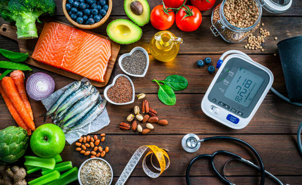Healthy food for heart care: overhead view of healthy food rich in Omega-3 and antioxidants and a blood pressure monitor, tape measure and stethoscope shot on wooden table. The composition includes a salmon fillet, sardines, avocado, extra virgin olive oil, brown lentils, celery, artichoke blueberries, celery, carrots, brown lentils, asparagus, artichoke, broccoli, flax seeds, chia seeds and some nuts like almonds, pistachio and pecan. High resolution 42Mp studio digital capture taken with SONY A7rII and Zeiss Batis 40mm F2.0 CF lens