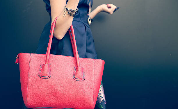 Fashionable beautiful big red handbag on the arm of the girl in a fashionable black dress, posing near the wall on a warm summer night. Warm color