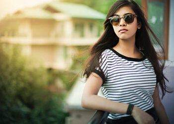 Outdoor image of beautiful, happy late teen urban girl enjoying fresh air in balcony at day time. She is wearing sunglasses, her long hair are flying in air. One person, horizontal composition with selective focus and copy space.