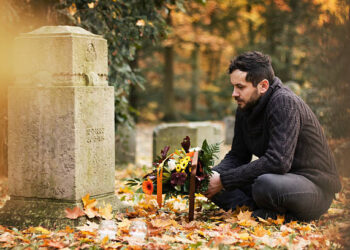 Mid adult man with flowers and candles visiting graves at the cemetery.