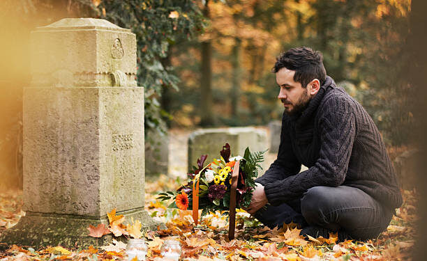 Mid adult man with flowers and candles visiting graves at the cemetery.